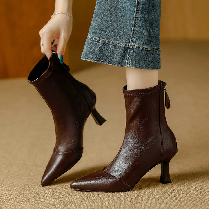 Mizuki chic pointed toe ankle boots in rich chestnut faux leather, shown from the side with a back zipper detail and stiletto heel as a hand pulls one boot on.
