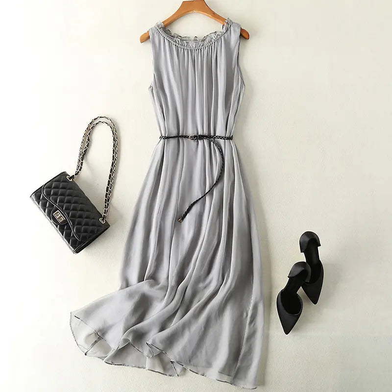 Muted grey pure silk midi slip dress, sleeveless design with ruffled neckline and braided belt, styled with a black quilted handbag and black stiletto heels.