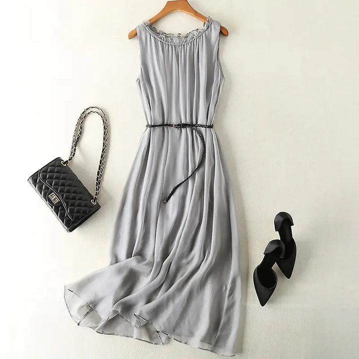 Muted grey pure silk midi slip dress, sleeveless design with ruffled neckline and braided belt, styled with a black quilted handbag and black stiletto heels.