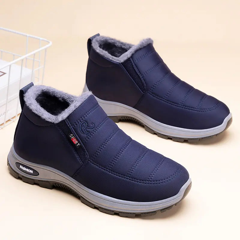 A pair of navy blue men's slip-on winter boots featuring quilted uppers, plush grey faux fur lining, and 'FASHION' lettering on the outsole. Shown from a three-quarter angle against a studio background.