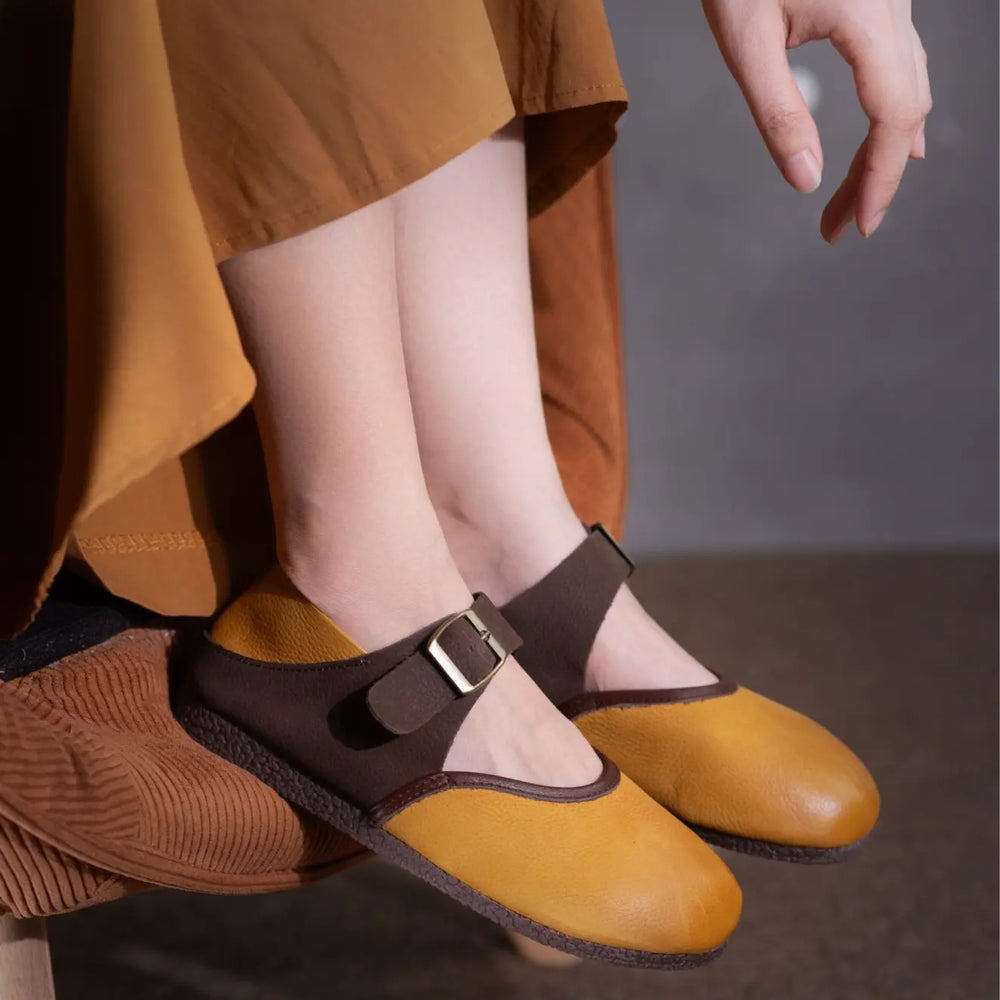 Chic two-tone nubuck leather Mary Jane flats in tan and coffee brown, featuring an adjustable buckle strap and round toe, shown styled on feet in a lifestyle setting.