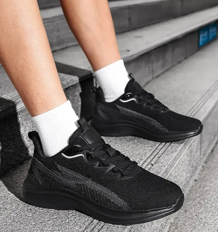 Black Nyrvix lightweight breathable running shoes worn by a person sitting on outdoor stairs, showcasing a three-quarter front view with white socks.