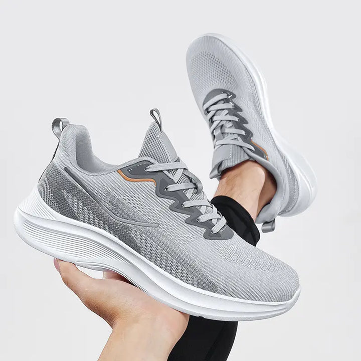 Nyrvix lightweight breathable running shoes in steel grey heathered knit with a sculpted white foam sole and orange accents, shown from a three-quarter angle.