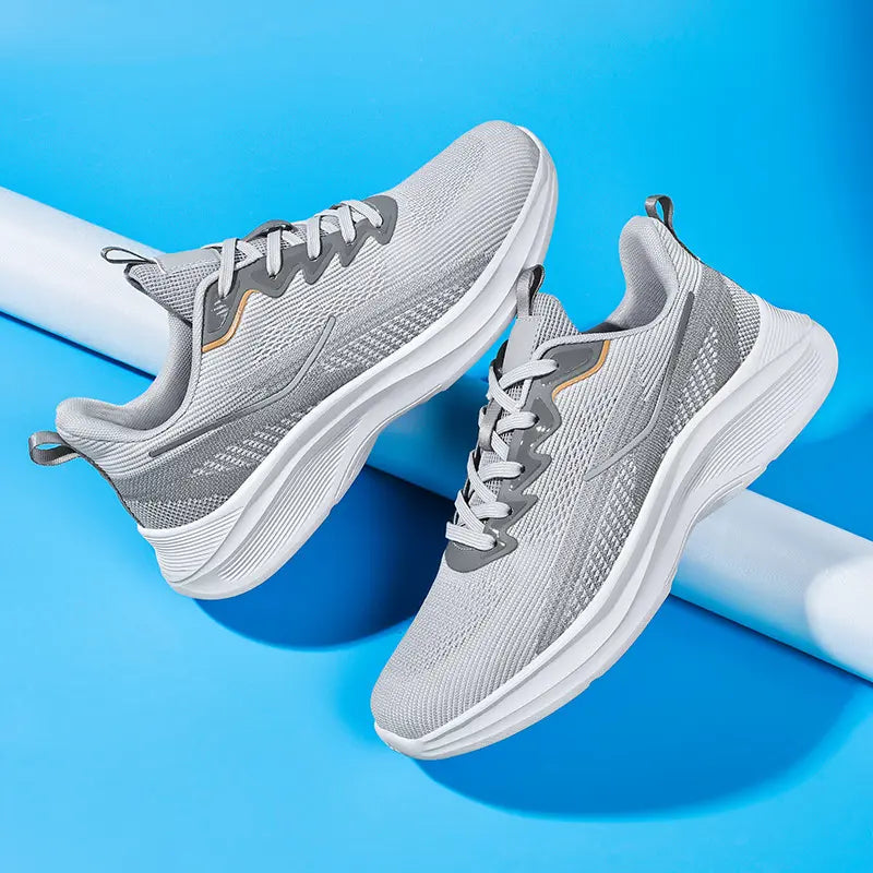 Two Nyrvix lightweight breathable running shoes in steel grey with white sculpted soles and subtle orange accents, displayed from a three-quarter angle on a vibrant blue studio background.