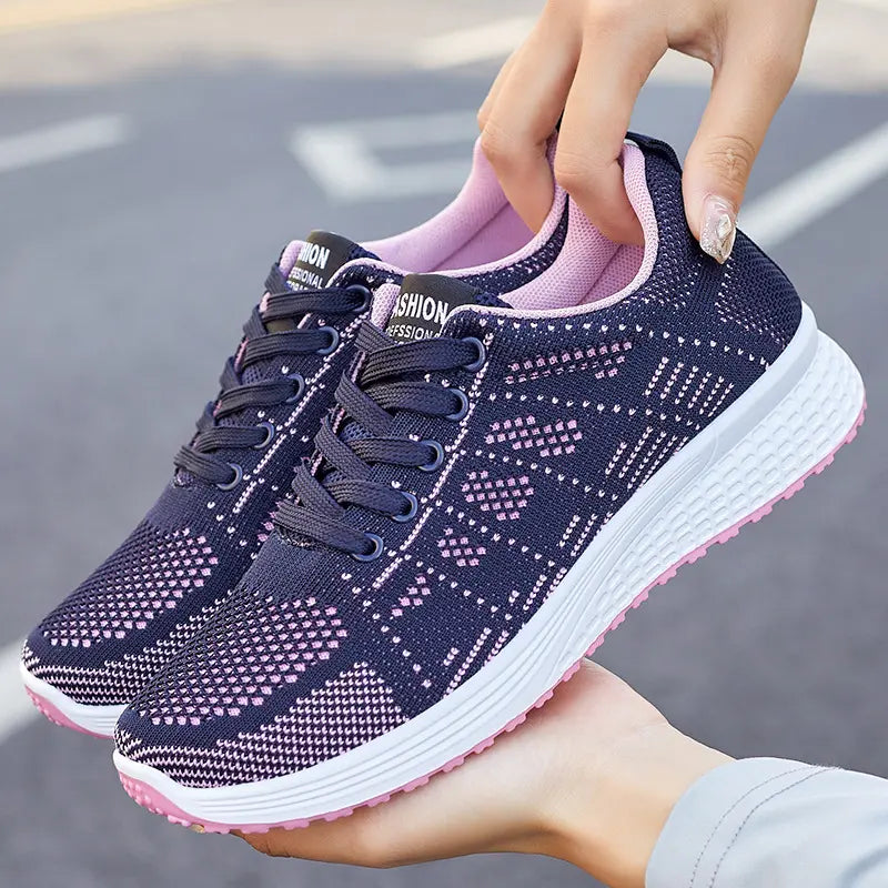 Navy blue knit low-top athletic sneakers with a delicate pink geometric pattern, pink lining and sole, and white midsole, held by hands.