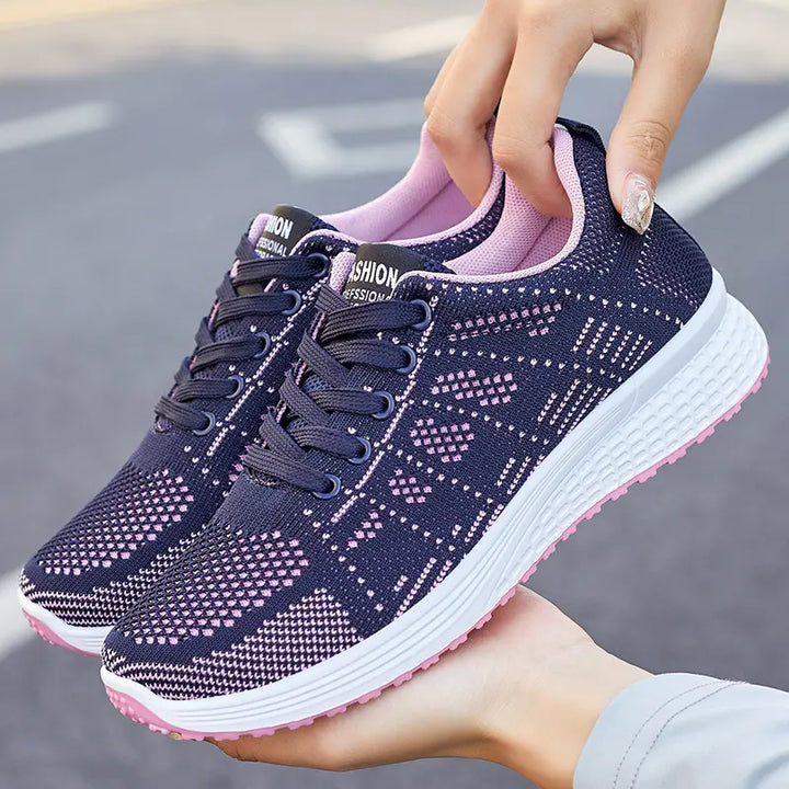 Navy blue knit low-top athletic sneakers with a delicate pink geometric pattern, pink lining and sole, and white midsole, held by hands.
