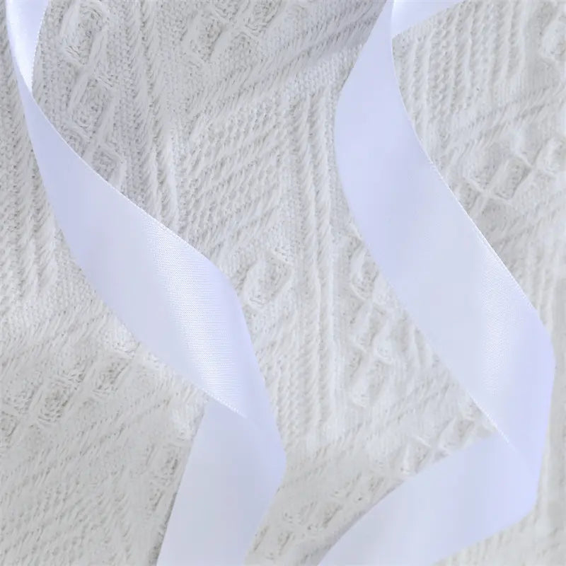 Close-up of intricate white floral lace fabric with two draped white satin ribbon ties, highlighting the delicate texture and smooth sheen of the Nyxos statement waist cincher accessory.