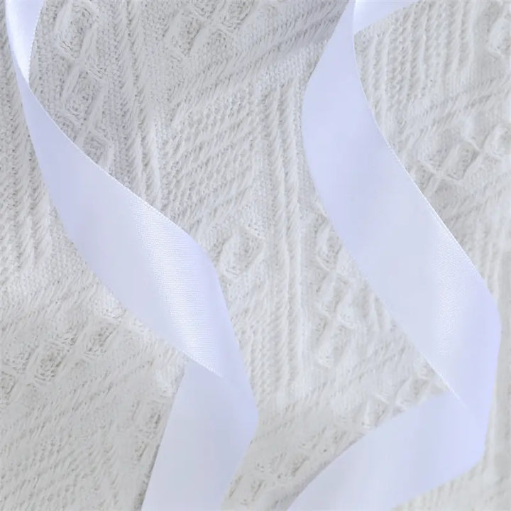 Close-up of intricate white floral lace fabric with two draped white satin ribbon ties, highlighting the delicate texture and smooth sheen of the Nyxos statement waist cincher accessory.