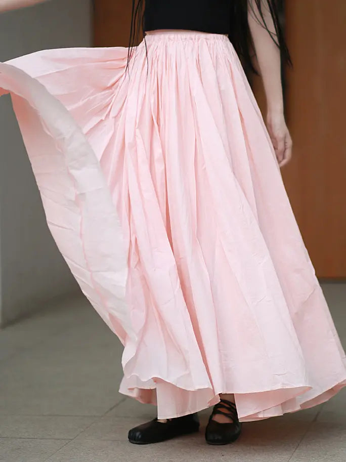 Flowing pale pink cotton maxi skirt worn by a model, showcasing its voluminous A-line silhouette and gathered elastic waistband in motion. This retro-inspired skirt drapes beautifully, perfect for bohemian and travel styles.