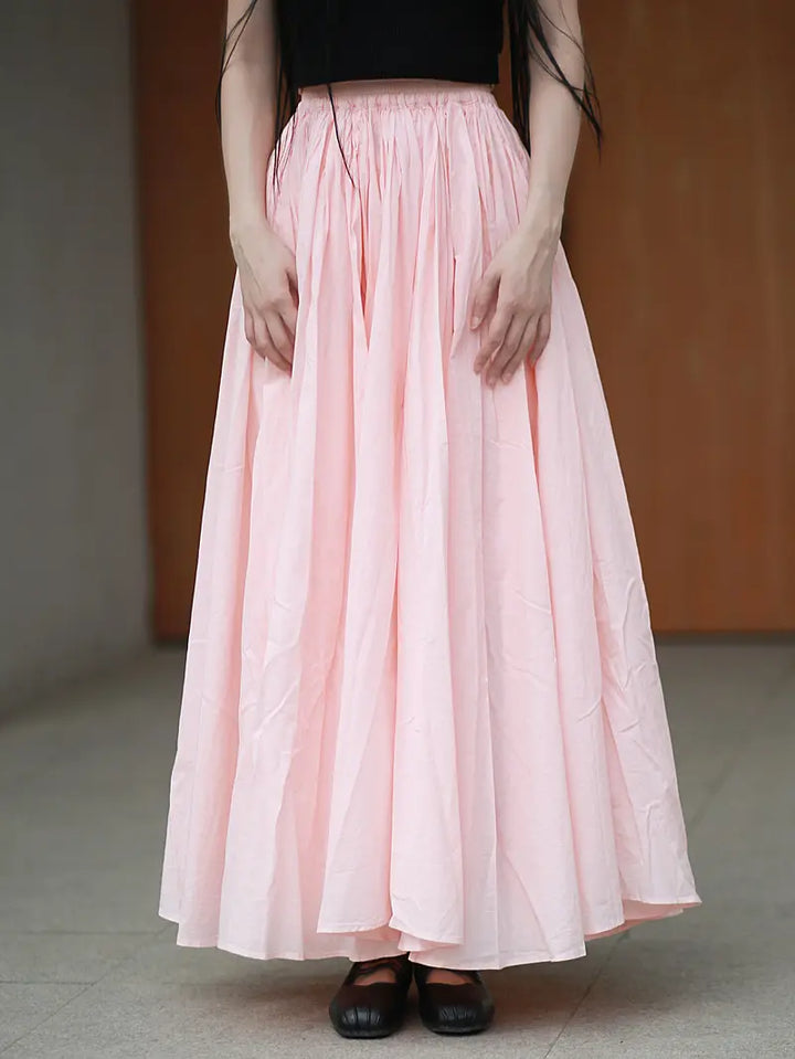 Full voluminous A-line maxi skirt in pale pink pure cotton, worn by a model from the waist down, showcasing its flowing silhouette and gathered elasticated waistband.