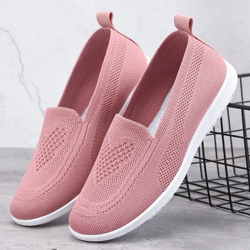 Pair of pink breathable knit slip-on trainers with a subtle diamond weave pattern on the vamp, a heel loop, and clean white soles.