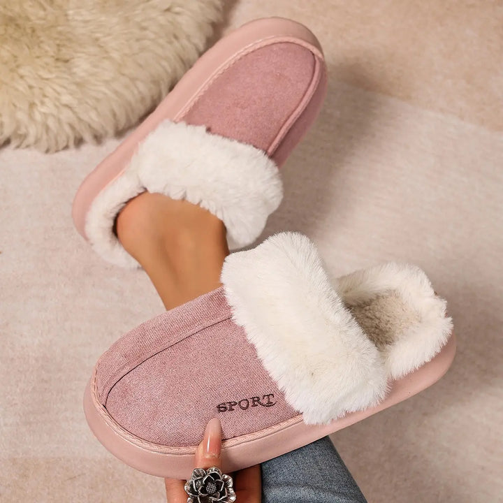 Plush pink mule slippers with white faux fur trim, shown on a foot with the embroidered &