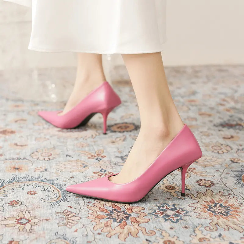 Pink high-gloss faux leather stiletto heels with a pointed toe and sculpted heel base, worn on a model&