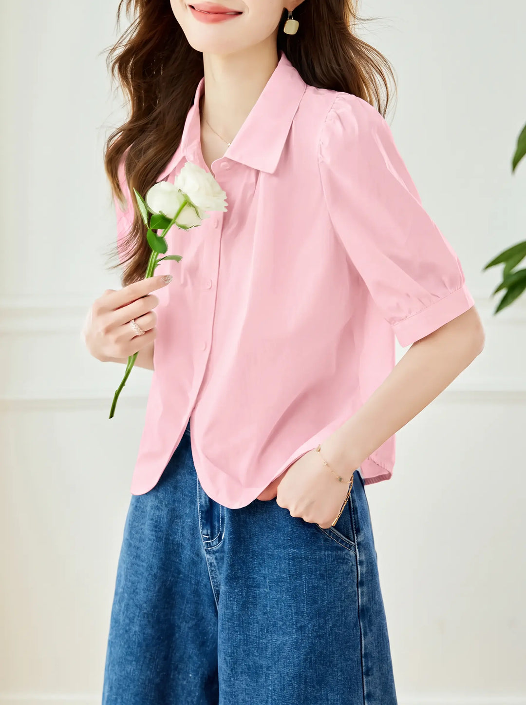 Women's pale pink short-sleeve blouse with puff sleeves, pointed collar, and a curved hem, styled with denim jeans.