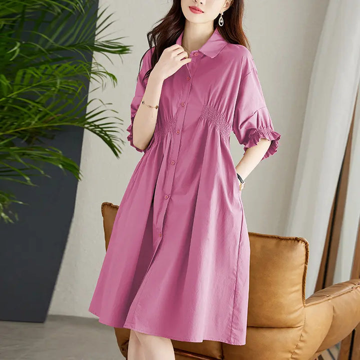Woman wearing a pink midi shirt dress featuring a shirred waist, classic shirt collar, button-front closure, and puffed sleeves with ruffled cuffs, shown in a lifestyle setting.