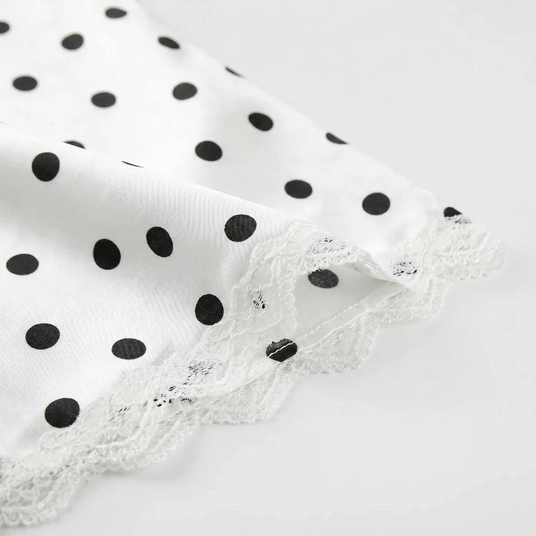 Close-up of white fabric with black polka dots and delicate white floral lace trim along the hem.