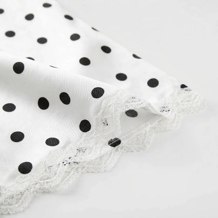 Close-up of white fabric with black polka dots and delicate white floral lace trim along the hem.