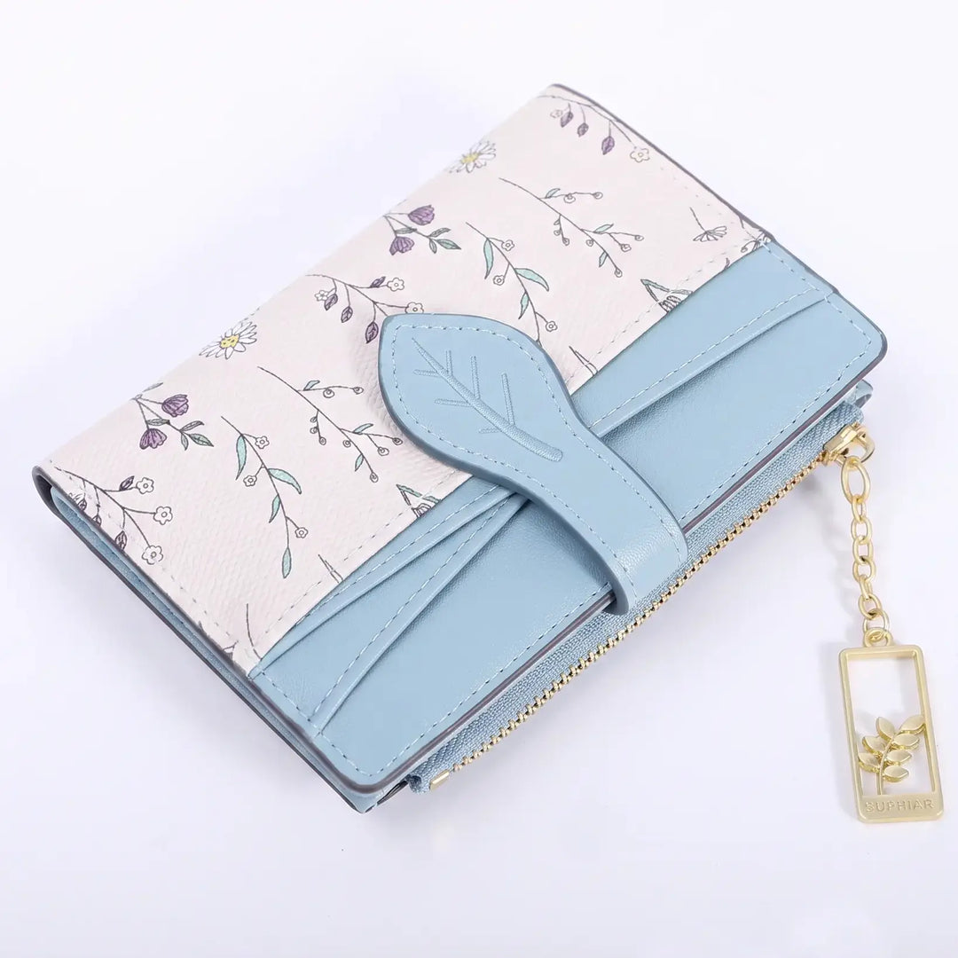Compact bi-fold wallet in Powder Blue with an off-white base adorned with a delicate floral print, featuring a light blue contrasting flap with a leaf-shaped closure and gold-tone hardware.