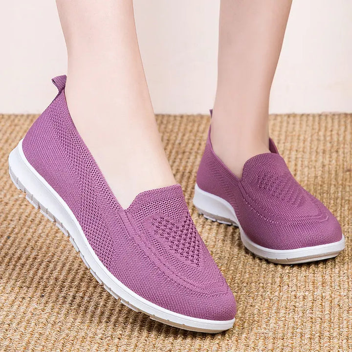 A pair of purple Zylos breathable knit slip-on trainers worn on feet, showcasing the subtle diamond weave pattern on the vamp and clean white sole.