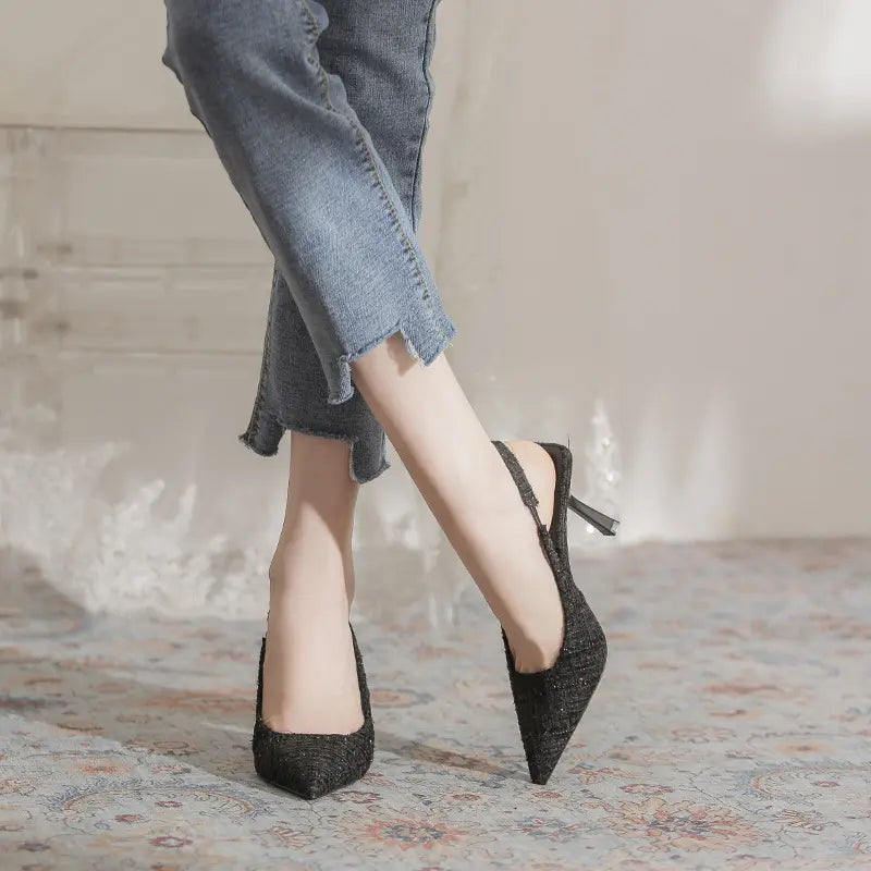 Chic Qalani black tweed-like pointed slingback heels worn by a model with cuffed jeans, showcasing the 7cm stiletto heel and adjustable buckle strap.