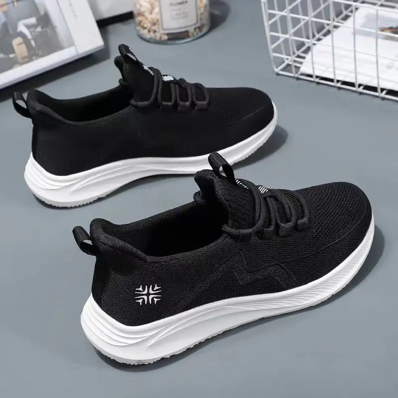 Two black breathable mesh athletic trainers with white sculpted soles, lace-up closure, and subtle wavy side detailing, shown from a three-quarter front view.