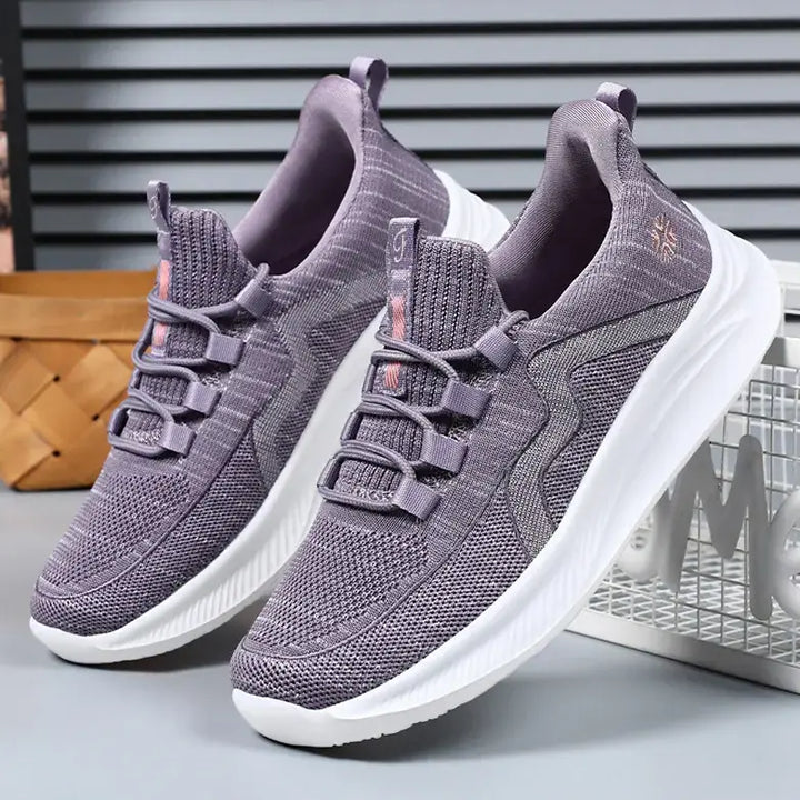 Pair of dusty rose breathable mesh athletic trainers with grey wavy side detail, flat laces, and white sculpted soles shown at a three-quarter angle.