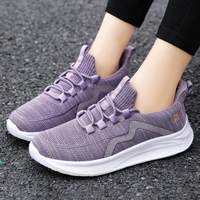 Women's Qanik breathable mesh athletic trainers in lilac purple, shown worn on feet with black trousers, featuring a wavy side graphic and white sculpted sole.