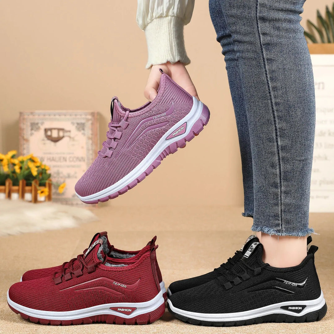 Three pairs of Qorto warm winter sneakers in purple, red, and black, shown at a three-quarter angle with a textured lifestyle background. The purple pair is held up, showcasing the knit upper and white midsole.