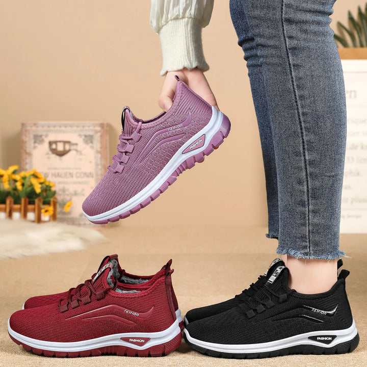 Three pairs of Qorto warm winter sneakers in purple, red, and black, shown at a three-quarter angle with a textured lifestyle background. The purple pair is held up, showcasing the knit upper and white midsole.