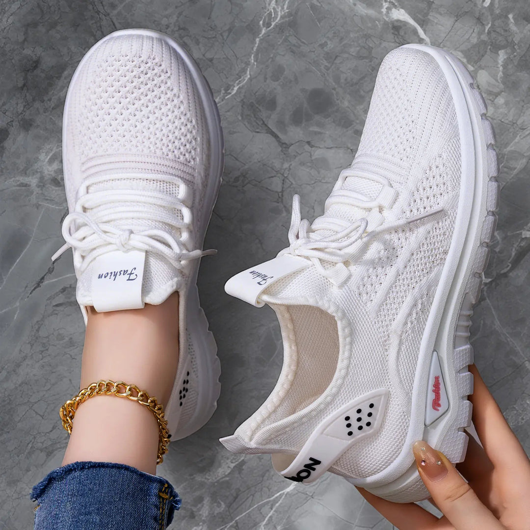 Flat lay of Raxen white breathable mesh sneakers, one shown on a foot with a gold chain, and the other held by a hand, on a grey marble background.
