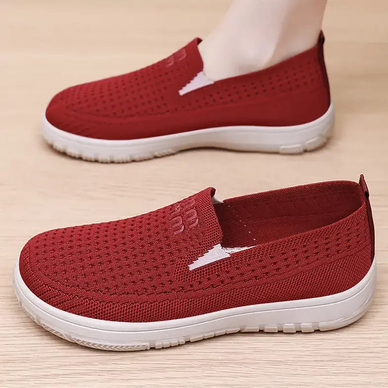 Red breathable flyknit mesh slip-on trainers for women, shown on a foot and flat lay on a wooden surface, featuring a cushioned white sole and subtle logo detail.
