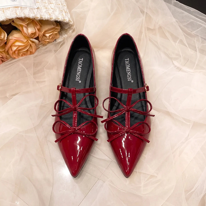 Pair of vibrant cherry red patent leather ballet flats with pointed toes, delicate multi-loop bows, and adjustable ankle straps.