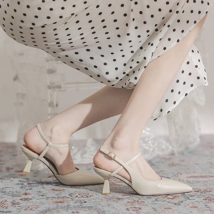Elegant ivory pointed-toe slingback heels with a sculptural flared mid-heel, shown on a model&