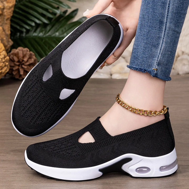 Black Rilux breathable knit slip-on sneakers worn on a foot, showcasing the air cushion sole and geometric knit pattern, styled with blue jeans and a gold ankle bracelet.