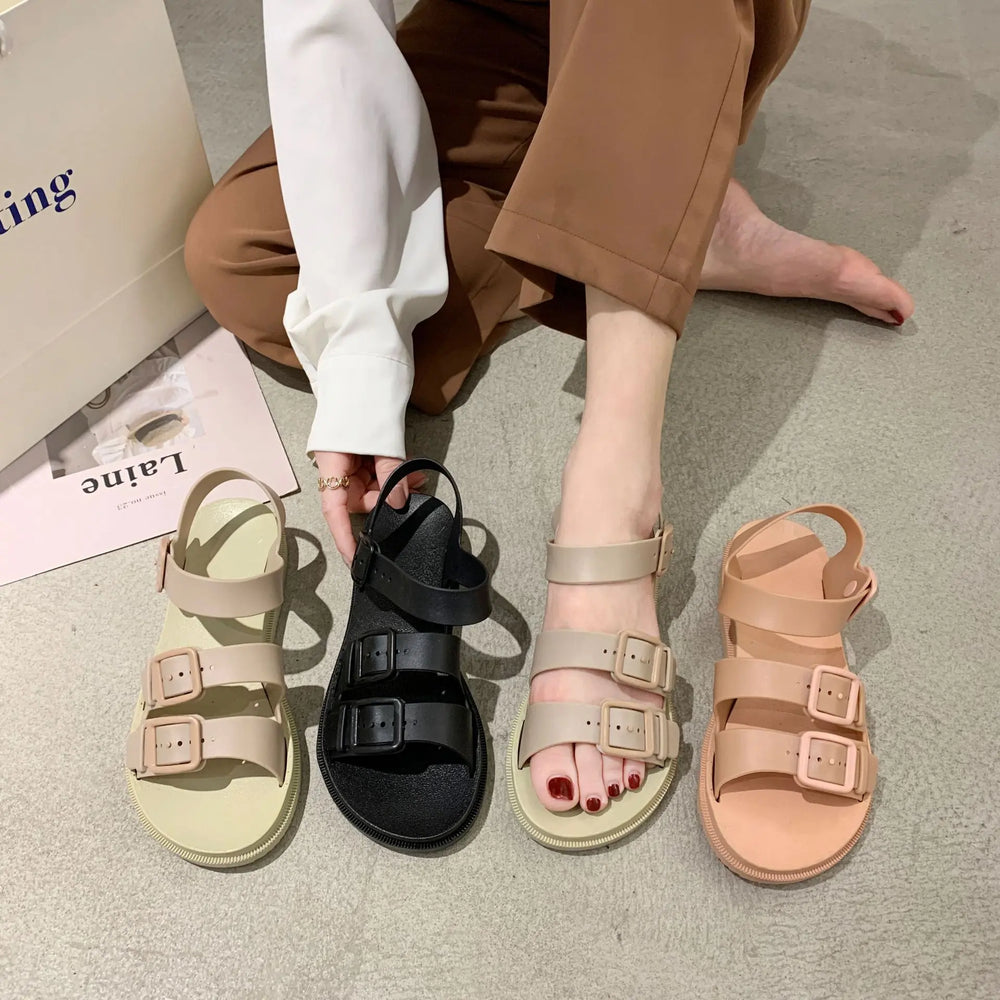Women's Rivenna platform slide sandals in black, taupe beige, and peach pink, featuring dual adjustable buckle straps and a low platform sole, shown with a person's legs and feet.