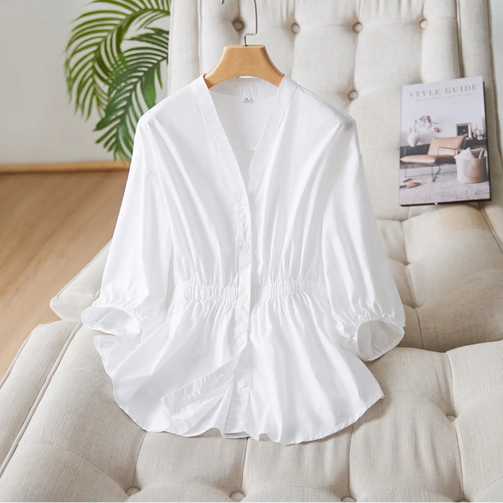 White Rixal V-neck cotton blouse with elasticated cinched waist and voluminous bubble sleeves, displayed on a hanger in a lifestyle setting.