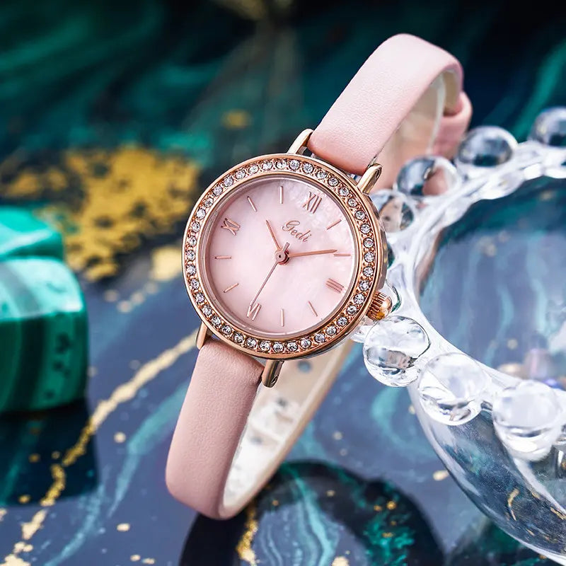 Elegant rose gold-plated ladies wristwatch with a soft pink dial, Roman numerals, and a sparkling cubic zirconia bezel, paired with a slim pink leather strap, presented against a dark, marbled background with decorative crystals.