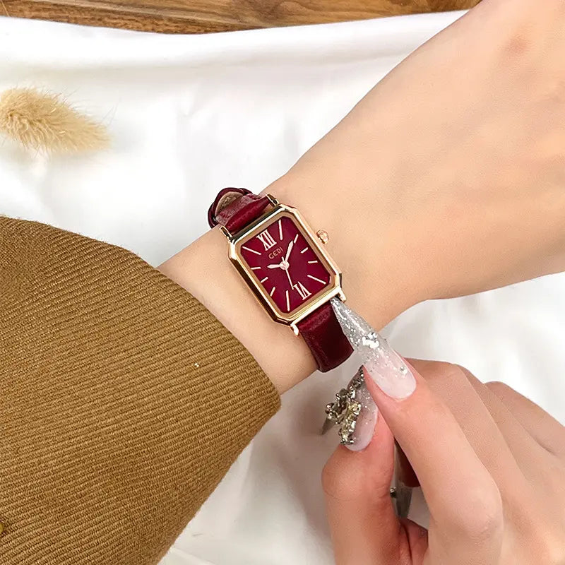 Elegant rose gold rectangular watch with a deep burgundy dial and matching faux leather strap featuring white contrast stitching, worn on a wrist.