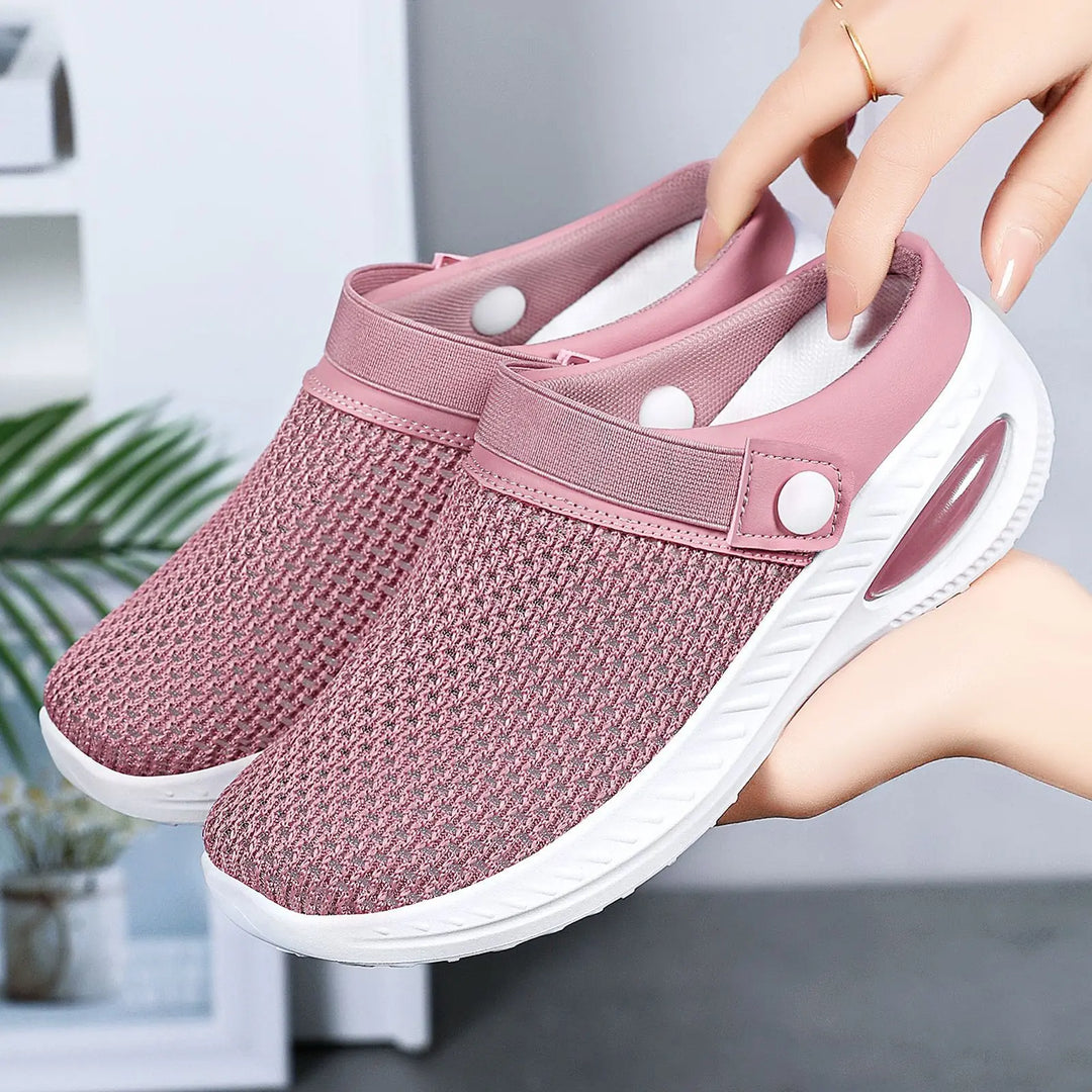 Rose pink breathable mesh slip-on clogs with white air cushion sole and adjustable button strap, held by hands in a studio setting.