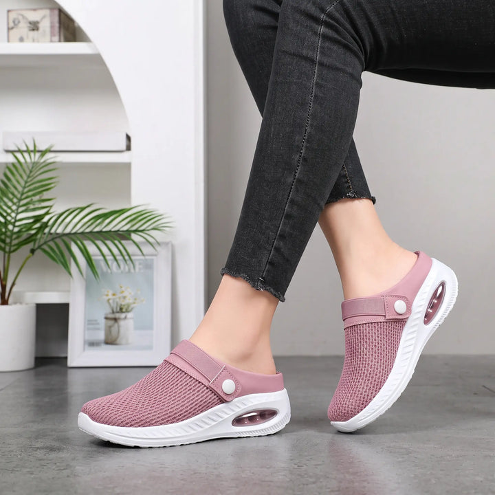 Rose pink breathable mesh slip-on clogs worn by a person, showcasing the side view of the comfortable, air-cushioned sole and adjustable button strap against a softly blurred indoor background.