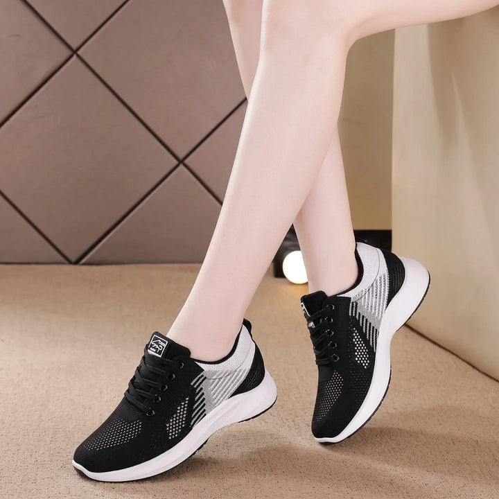 Rylux breathable knit sneakers for women, shown in black with white soles, worn by a model in a lifestyle shot. Features lightweight construction and a secure lace-up closure.