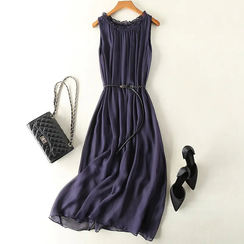 Muted grey pure silk midi slip dress with ruffled neckline and braided belt, styled with a quilted handbag and black heels on a white background.