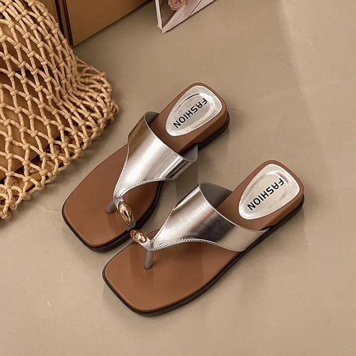 Silver square-toe thong sandals with a brown footbed and a gold-tone knot embellishment, featuring visible &