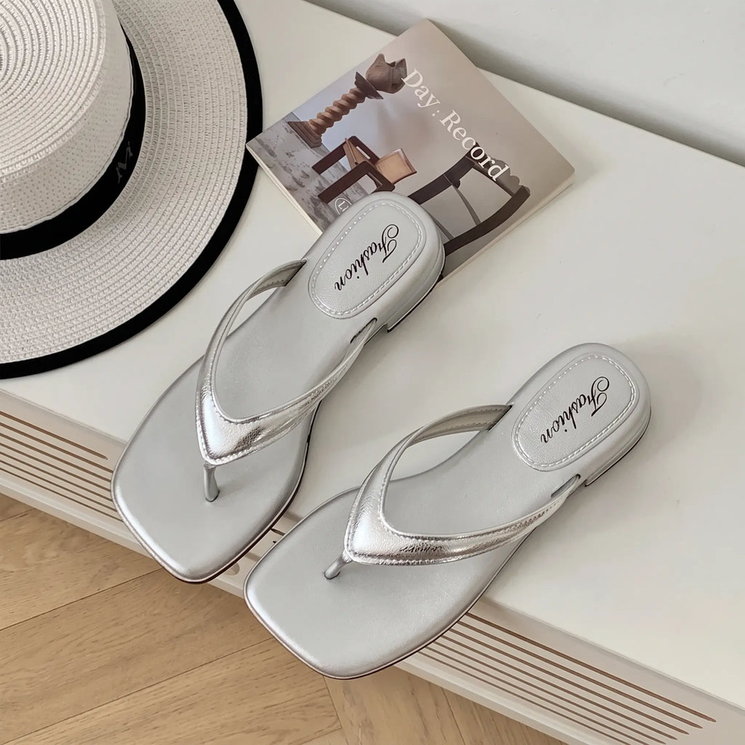 Pair of shimmering silver square-toe thong sandals with a low wedge heel, featuring embossed &