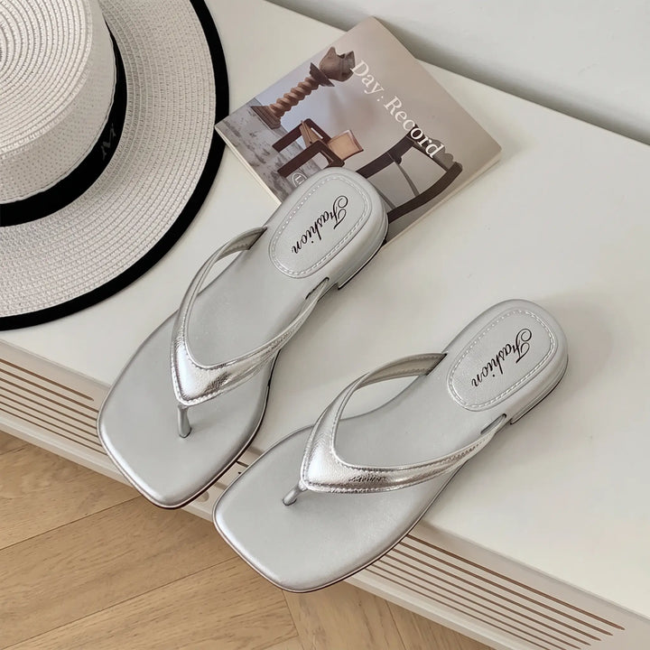 Pair of shimmering silver square-toe thong sandals with a low wedge heel, featuring embossed &