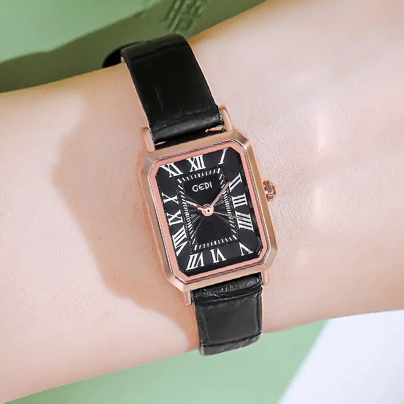 Tarkhan rectangular rose gold watch with a black dial, Roman numerals, blue hands, and a black embossed leather strap worn on a wrist. Elegant accessory for women.