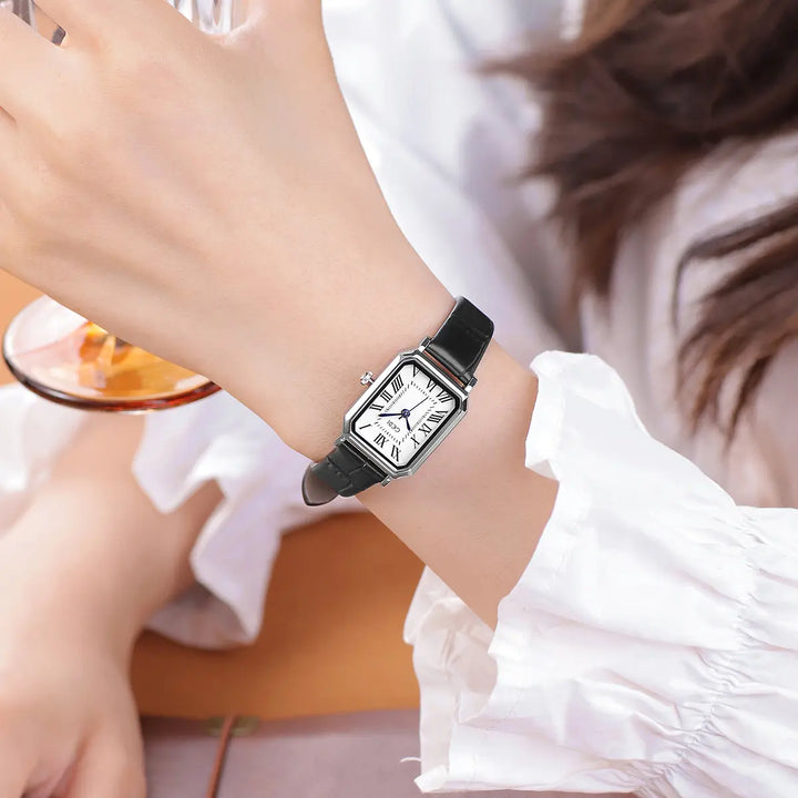 Elegant rectangular rose gold watch with a white dial, Roman numerals, and blue hands, worn on a wrist with a black leather strap.