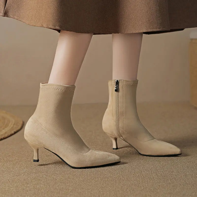 Chic taupe beige stretch ankle boots with pointed toes and slender stiletto heels, worn by a model in a lifestyle setting, showcasing a sophisticated everyday look.