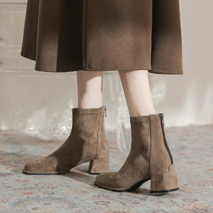Chic taupe suede-like ankle boots with square toes and back zippers, styled with a long brown skirt for a sophisticated winter look.