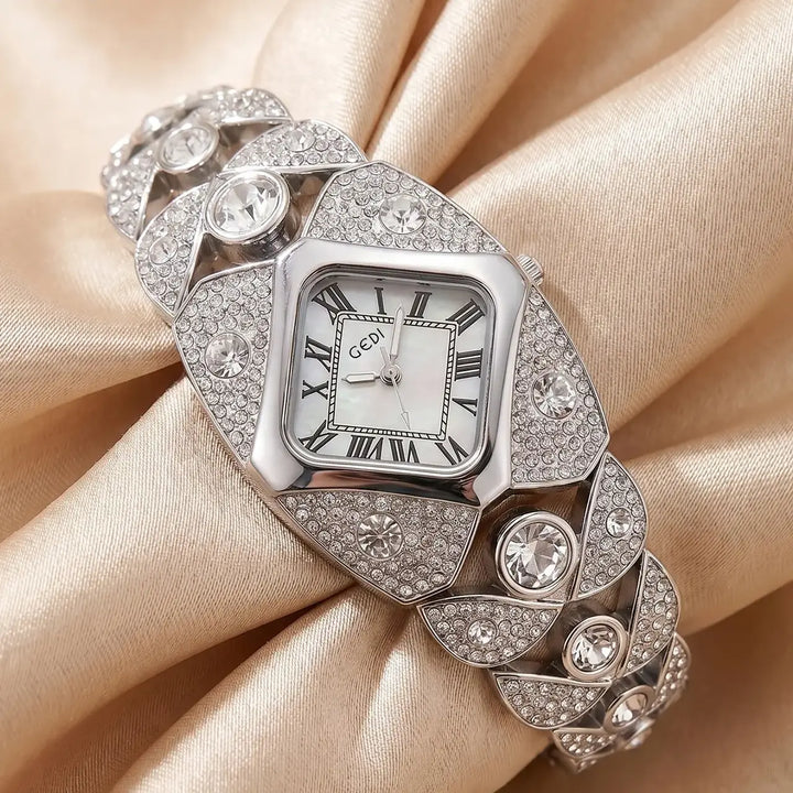 Silver-tone Tavril diamond-embellished bracelet watch featuring a rhombic case with Roman numerals on a mother-of-pearl dial, set on a satin fabric.